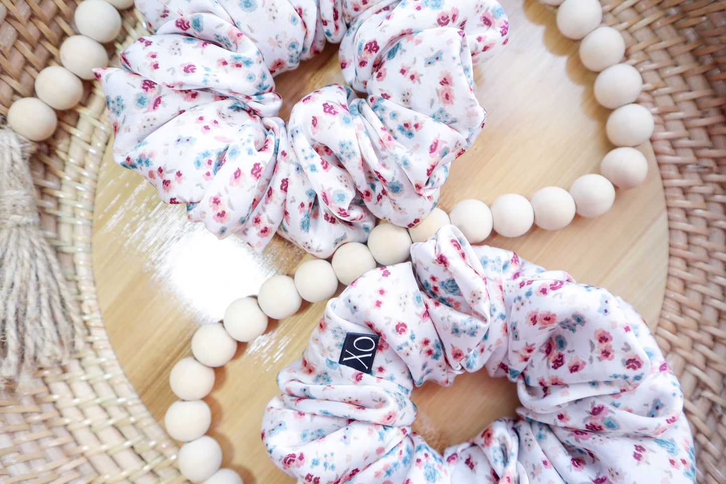 Floral scrunchies on a wooden surface with a wooden bead. Scrunchie fabric in photo looks brighter due to lighting.