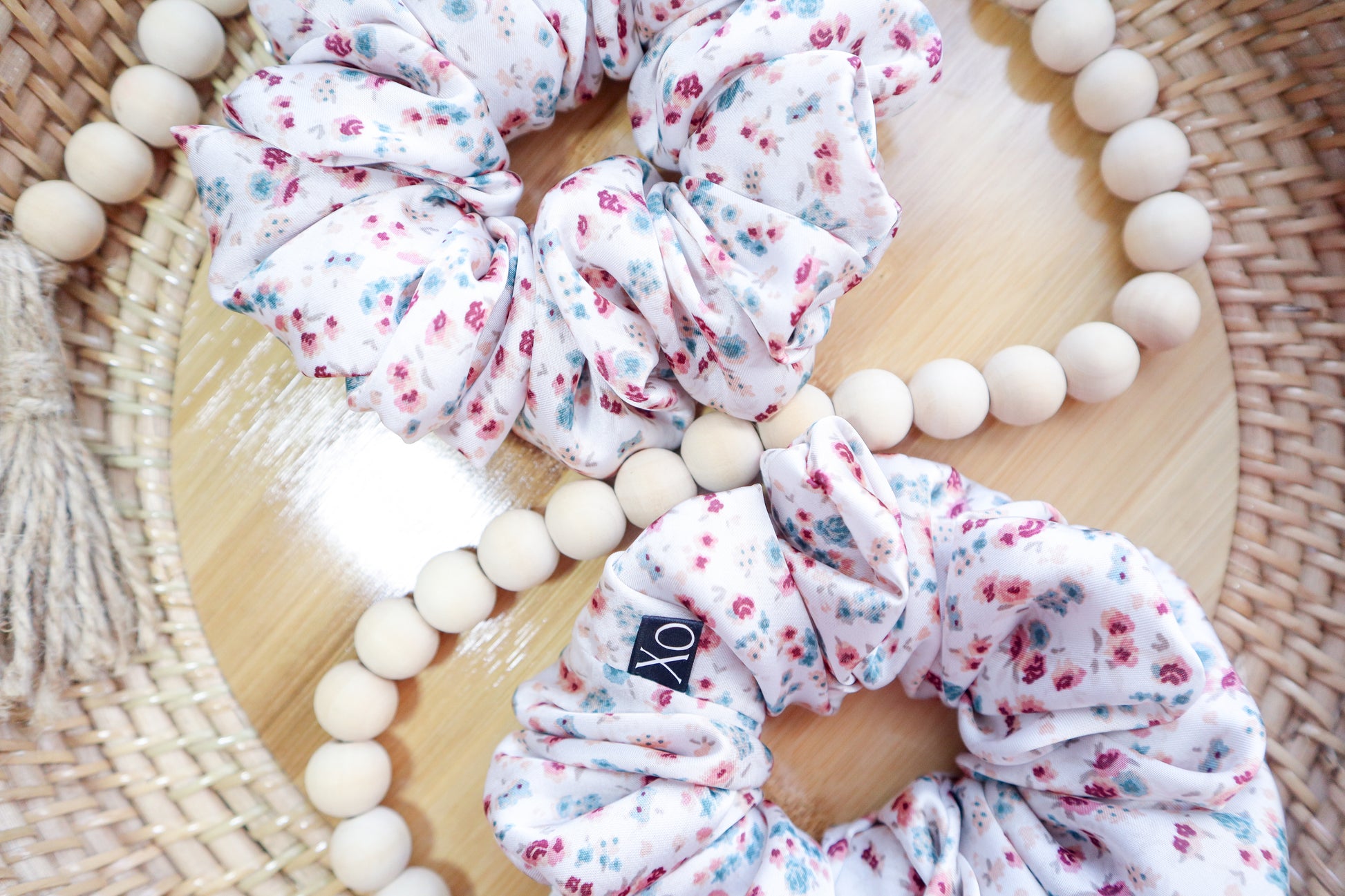 Floral scrunchies on a wooden surface with a wooden bead. Scrunchie fabric in photo looks brighter due to lighting.