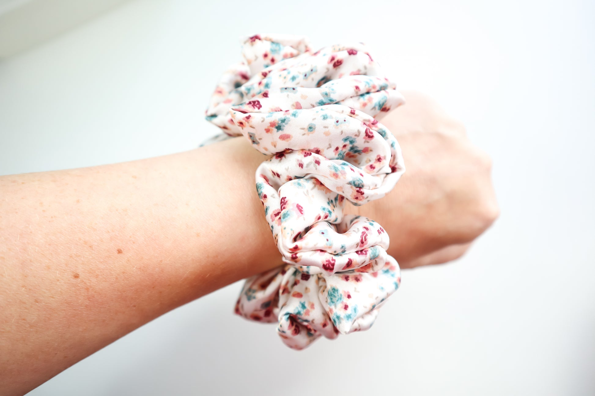 Floral scrunchies worn on wrist against a white background