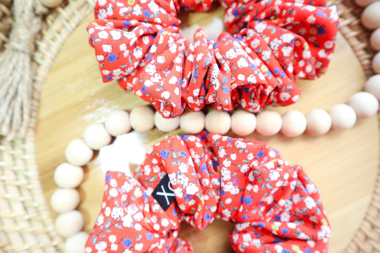 Red floral scrunchies on a wooden surface with beads. Fabric color shown in photo looks lighter due to lighting.