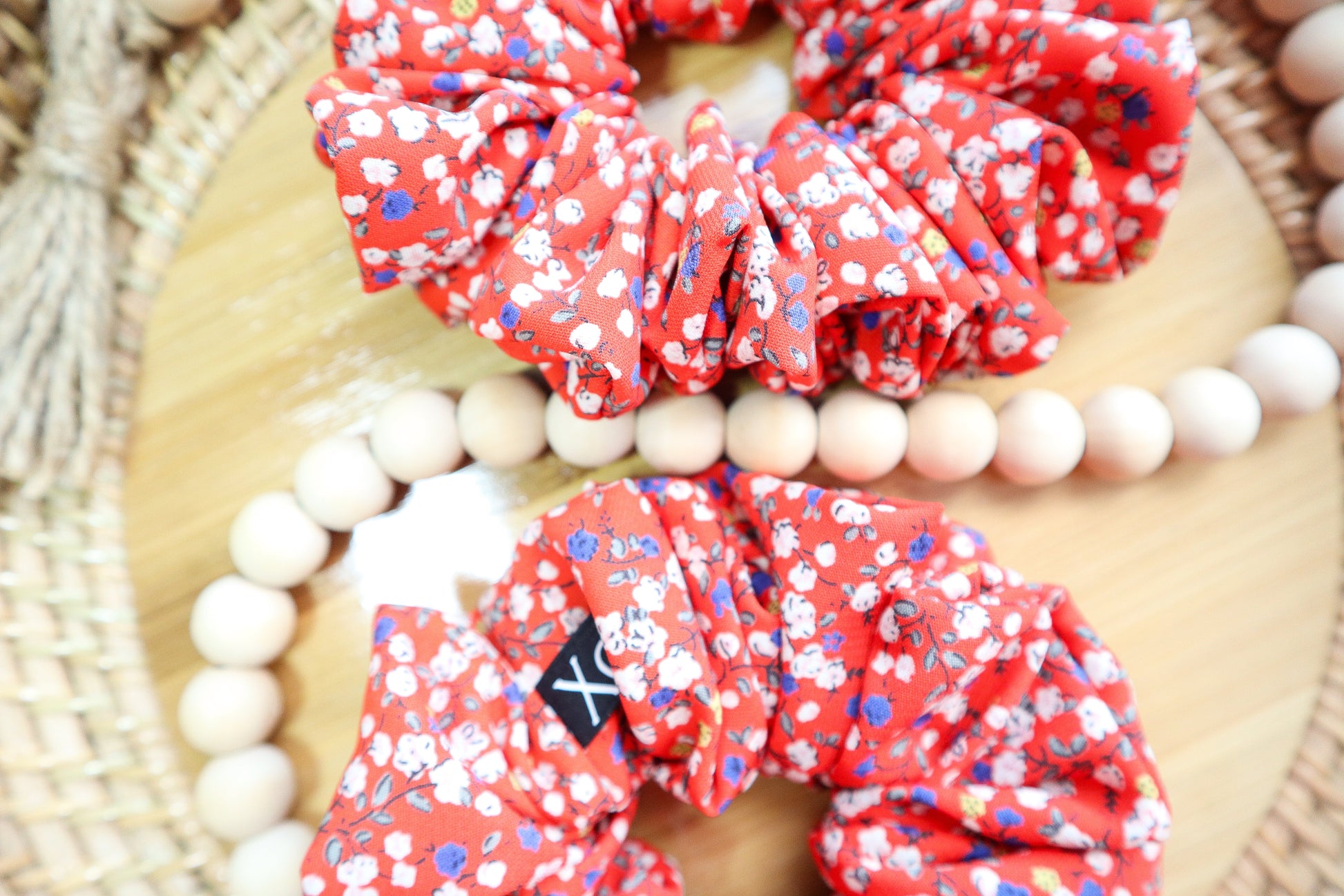 Red floral scrunchies on a wooden surface with beads. Fabric color shown in photo looks lighter due to lighting.