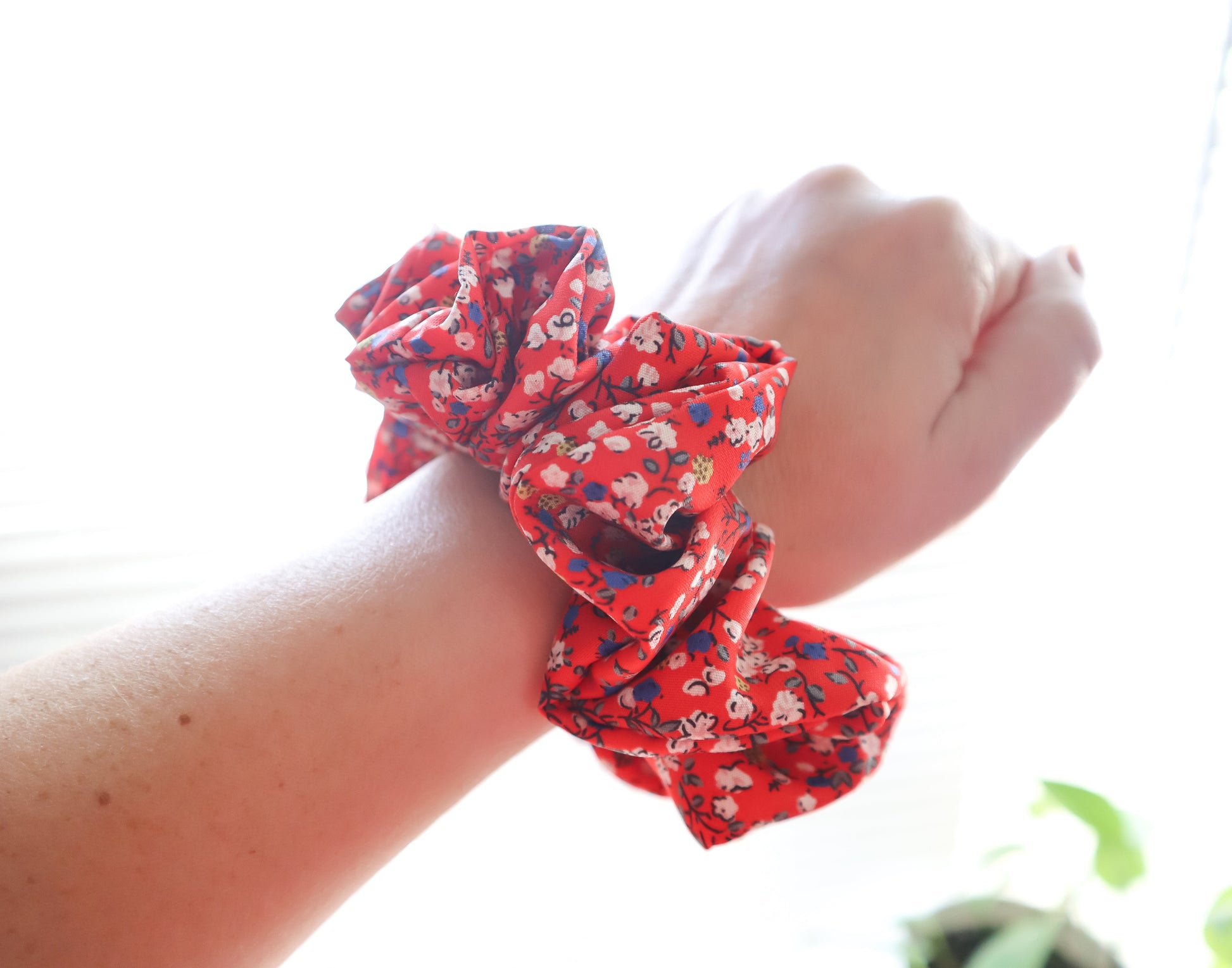 Red floral scrunchie on a wrist with a blurred background