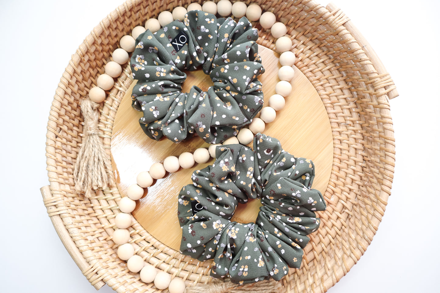 Two gray scrunchies with a floral pattern on a woven plate with wooden beads.