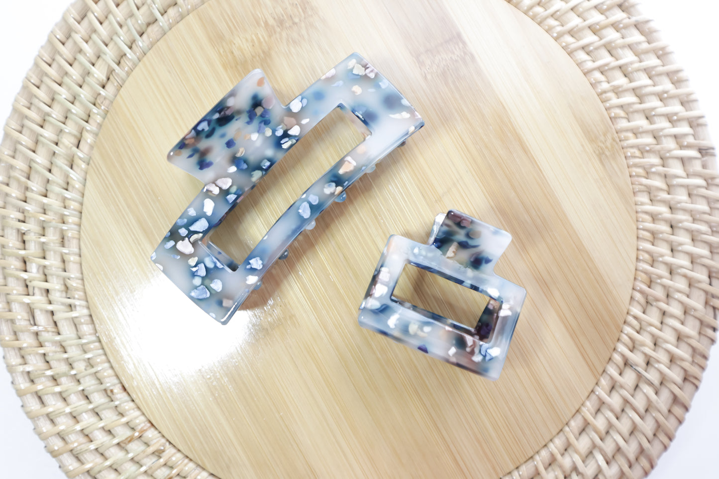 Two square hair clips with a marbled design on a woven mat.