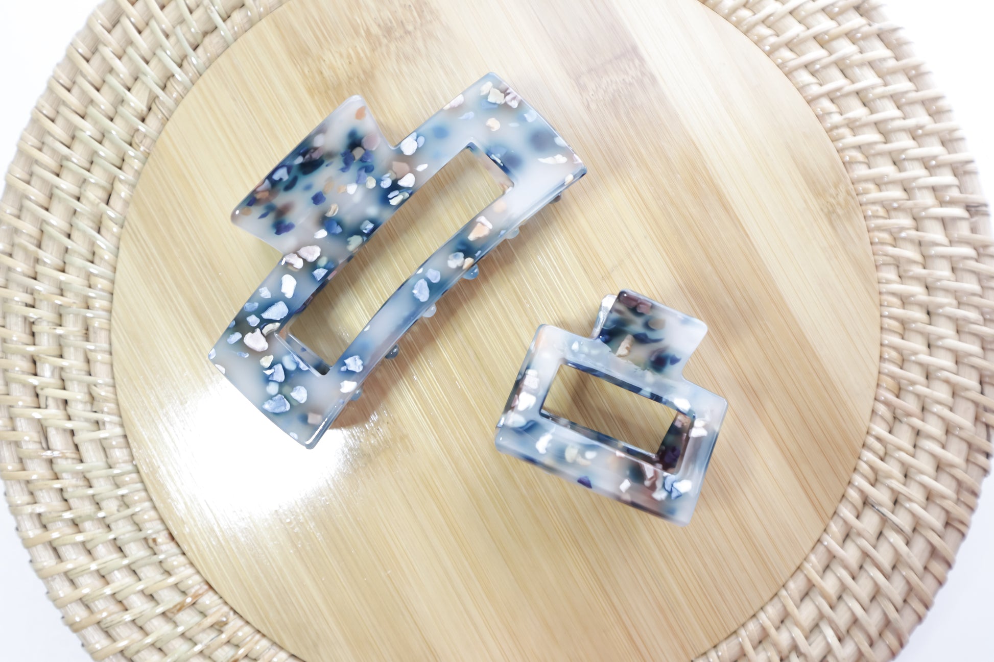 Two square hair clips with a marbled design on a woven mat.
