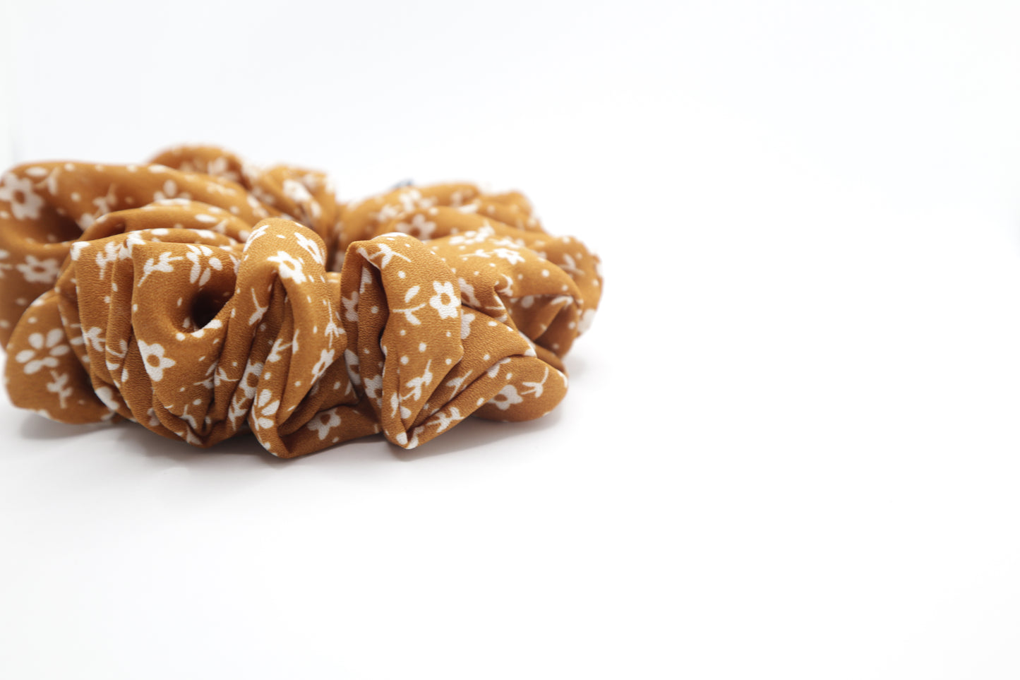 Brown scrunchie with white floral pattern on a white background