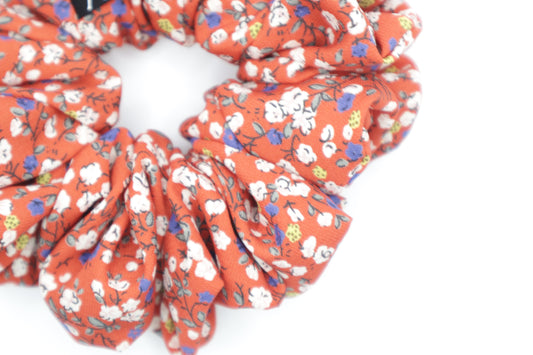 Red floral scrunchie on a white background. Fabric in this photo is less bright due to lighting.
